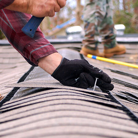 A roofer applies shingles to roof ridge.